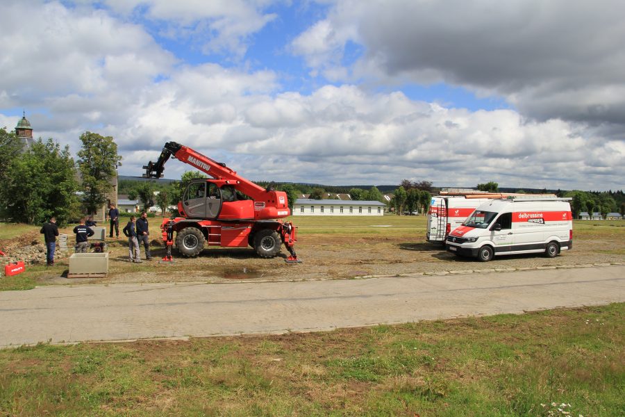 Technicien Delbrassine effectuant une installation sanitaire extérieure sur des tuyaux d'évacuation en PVC.